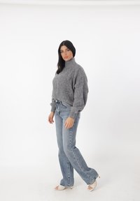 Grijze gebreide coltrui met een losse pasvorm en geribbelde manchetten, gecombineerd met lichtblauwe flared jeans en witte blokhak sandalen.