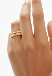 Anillos de metal dorado apilados en un dedo; uno tiene una superficie lisa y el otro presenta una textura estriada para contraste.