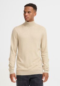 Pulover bej cu guler înalt, din material tricotat cu striații, având mâneci lungi și un design ajustat. Textură netedă și ușor elastică.