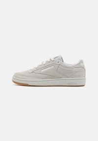 Zapatillas de ante gris claro con un logo blanco, suela de goma plana y puntera redondeada. Presentan detalles de costura y diseño con cordones.
