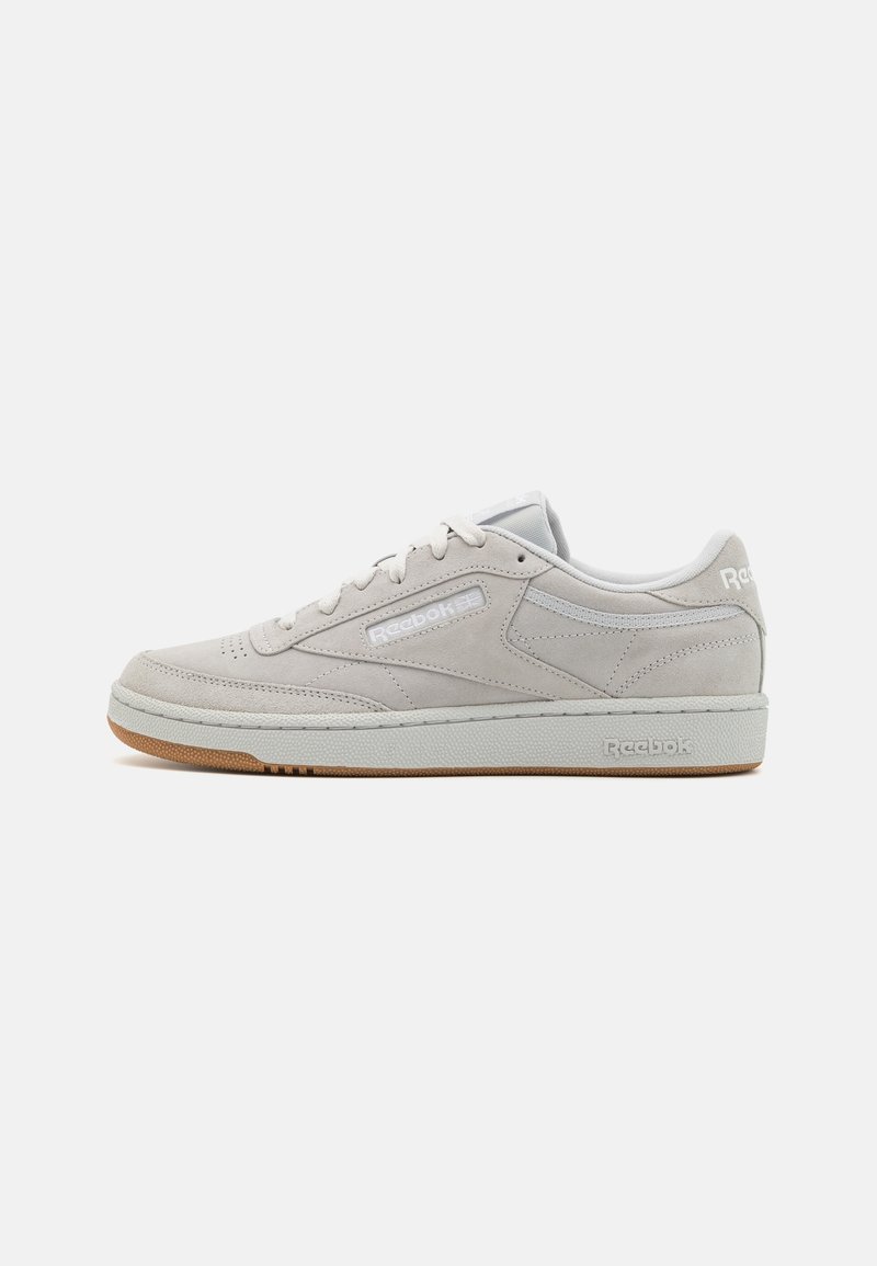 Zapatillas de ante gris claro con un logo blanco, suela de goma plana y puntera redondeada. Presentan detalles de costura y diseño con cordones.