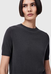 Kortærmet, mørkegrå sweater lavet af blødt stof. Har en rund halsudskæring og en glat tekstur med subtile ribbede detaljer ved kanterne.