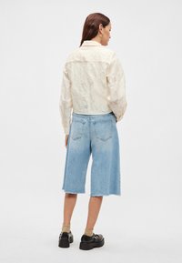 Kremowa kurtka o fakturze, z kołnierzem, w połączeniu z jasno niebieskimi spódnicami jeansowymi do kolan z postrzępionymi brzegami. Całość dopełniają czarne buty na platformie.