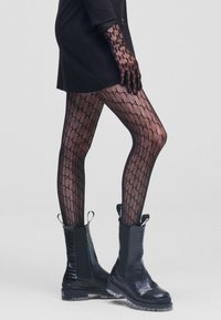 Le calze nere a fantasia presentano un design geometrico. Abbinato a stivali neri lucidi alla caviglia con texture in coccodrillo e suola spessa.