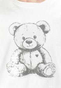 T-shirt blanc avec un ours en peluche illustré gris, un cœur et des accents de sequins, en tissu doux avec un col rond.