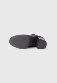 Suela de zapato negra con una parte inferior de goma texturizada, que presenta un patrón estriado para mejorar el agarre y un diseño de tacón ligero.