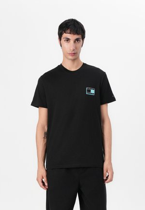 T-shirt en coton noir avec un petit logo multicolore sur la poitrine gauche, col rond, manches courtes, associé à un pantalon noir.