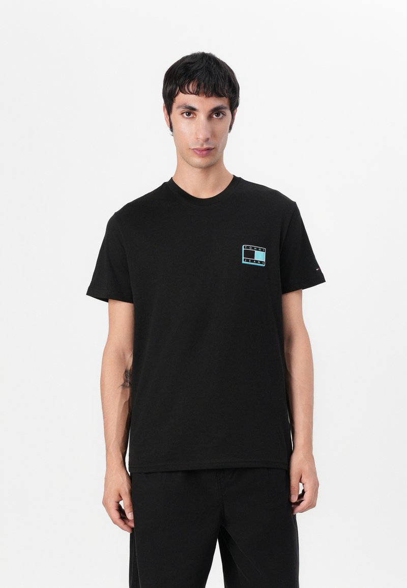 T-shirt en coton noir avec un petit logo multicolore sur la poitrine gauche, col rond, manches courtes, associé à un pantalon noir.