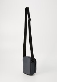 Borsa a spalla in tessuto nero con una texture liscia, forma rettangolare, chiusura con zip e tracolla regolabile con lettering in rilievo.