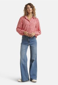 Pink button-up shirt with heart pattern, long sleeves, elastic cuffs; paired with light blue wide-leg jeans and white shoes.