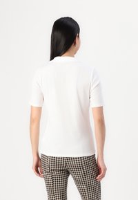 Hvid polo t-shirt med korte ærmer, klassisk krave, glat tekstur og tætsiddende pasform, parret med sort-hvide ternede bukser.