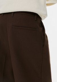 Brązowe spodnie w eleganckim stylu, charakteryzujące się gładką fakturą, kieszeniami bocznymi oraz jedną tylną kieszenią o smukłym fasonie. Klasyczny krój i wykończenie.