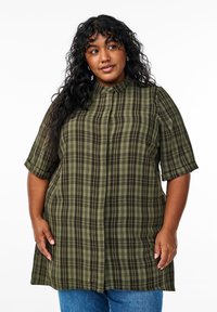 Camisa de cuadros verde y marrón con mangas cortas, un cuello alto y botones en la parte frontal. La tela parece estar tejida con una textura suave.