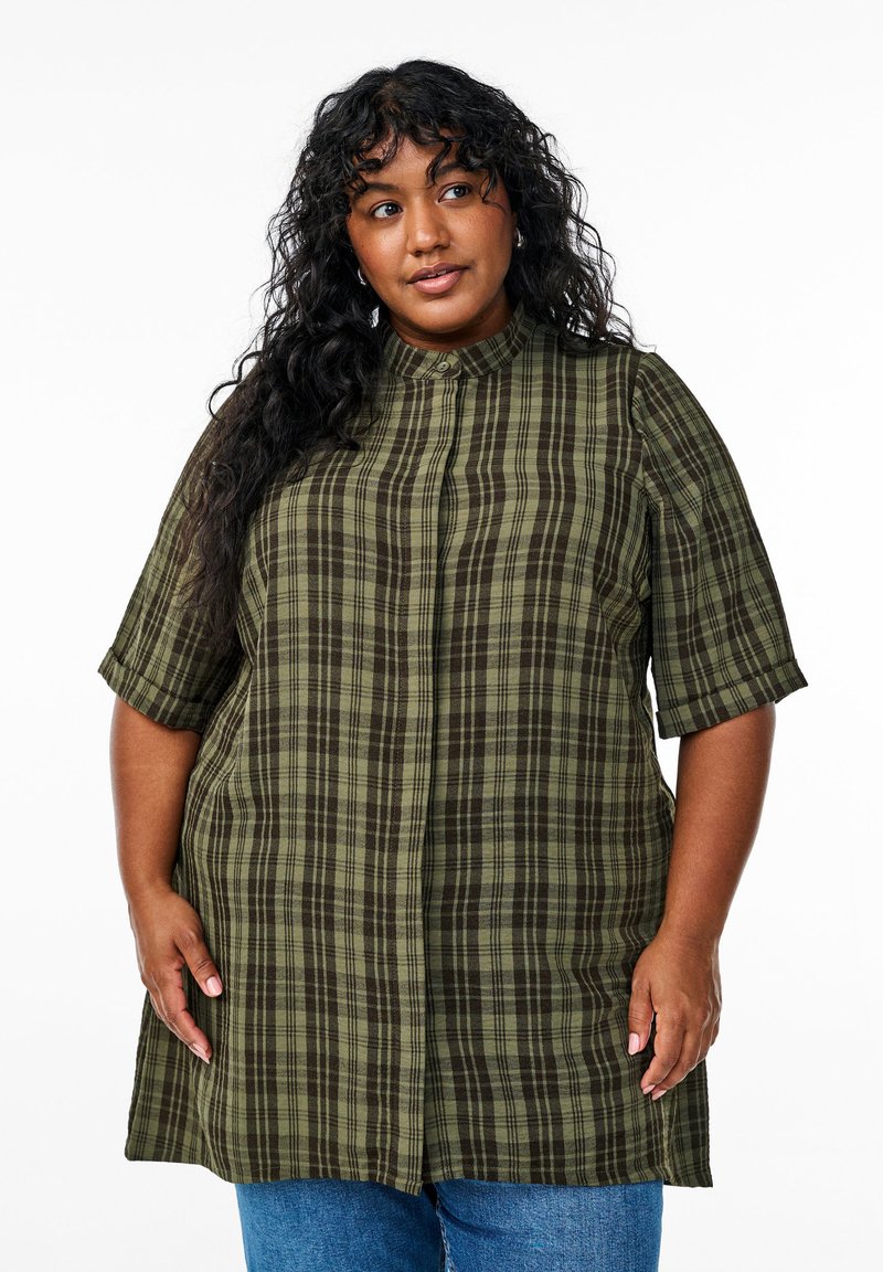 Camisa de cuadros verde y marrón con mangas cortas, un cuello alto y botones en la parte frontal. La tela parece estar tejida con una textura suave.