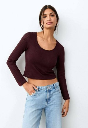 Bordeauxrotes, langärmliges, geripptes Oberteil mit Rundhalsausschnitt und kurzem Schnitt, kombiniert mit hellblauen, hoch taillierten Jeans.