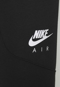 Svart tyg med vit Nike Air-logga tryckt ovanför en böjd söm.