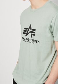 Lys grøn kortærmet t-shirt med et sort grafisk logo med kantet design og brandtekst. Blødt stof med en afslappet pasform.