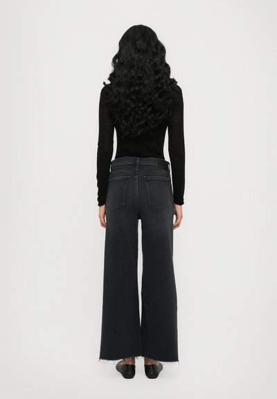 Jeans large taille en denim foncé avec ourlet effiloché et design classique de poches arrière. Associés à un haut noir ajusté à manches longues.