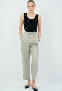 Černý tops bez rukávů s bílými puntíky, spárovaný se světle šedými kalhotami se strečovým pasem a bočními kapsami. Černé ploché boty.