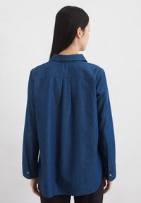 Tume sinine denim särk pikkade varrukatega, krae ja ühe nupuga mansetid. Tagaküljel on lisaliikumiseks plekk.