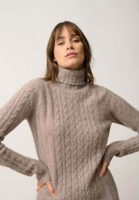 Maglione in cable-knit beige chiaro con colletto alto. Texture morbida e polsini a coste. Motivo a treccia ben visibile lungo il corpo.