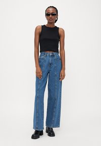Top nero senza maniche abbinato a jeans ampi blu. I jeans presentano cuciture frontali e sono abbinati a stivali piattaforma neri chunky.
