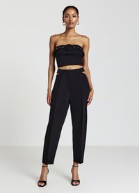 Ensemble deux pièces noir comprenant un haut sans bretelles avec un accent circulaire et un pantalon taille haute bien ajusté. Tissu lisse avec des côtés découpés.