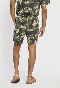 Camo-patterned shorts in shades of green and beige, featuring an elastic waistband and a relaxed fit. Textured fabric, above-the-knee length.