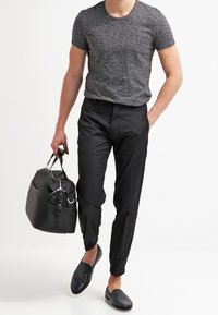 Camiseta de algodón ligera y negra con un patrón texturizado, combinada con pantalones negros ajustados y llevando un bolso de viaje negro. Zapatos negros sin cordones.