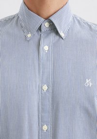 Blue and white striped button-up shirt with a classic collar, featuring white buttons and a small embroidered logo on the chest.