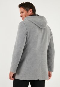 Šedý kabát s kapucí z hebké látky, s hladkým povrchem, střižený na míru a s jemnými švy na zadní straně.