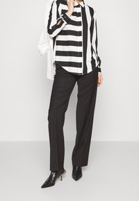 Schwarz-weiß gestreiftes Hemd mit Kragen, kombiniert mit maßgeschneiderten schwarzen Hosen und spitzen schwarzen High Heels. Hat ein klassisches, strukturiertes Design.