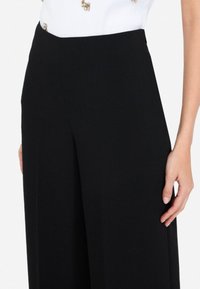 Pantalones de pierna ancha negros con una textura suave y un corte entallado, que cuentan con una cintura alta y bolsillos laterales, adecuados para diversas ocasiones.