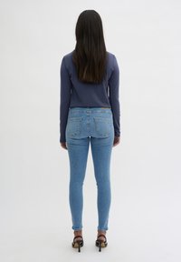 Langärmliges blaues Oberteil kombiniert mit hellblauen Jeans. Die Jeans bieten eine schlanke Passform und haben zwei Gesäßtaschen. Schwarze High-Heels runden das Outfit ab.
