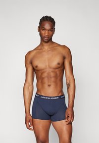 Boxeri din bumbac de culoare albastru închis, cu un brâu lat negru ce prezintă litere albe "JACK & JONES". Textură netedă și design ajustat.