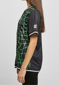 Maglia nera con motivo a rete verde, maniche corte, dettagli a righe bianche sul colletto e sull'orlo, materiale sintetico liscio.