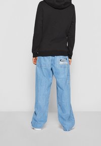 Černá mikina s kapucí a volným střihem, doplněná světle modrými džínovými cargo kalhotami s logem a bočními kapsami.