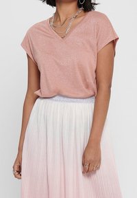 Top de cuello en v glitter rosa con mangas cortas, combinado con una falda plisada que se desvanece de blanco a rosa claro, con una cinturilla plateada.