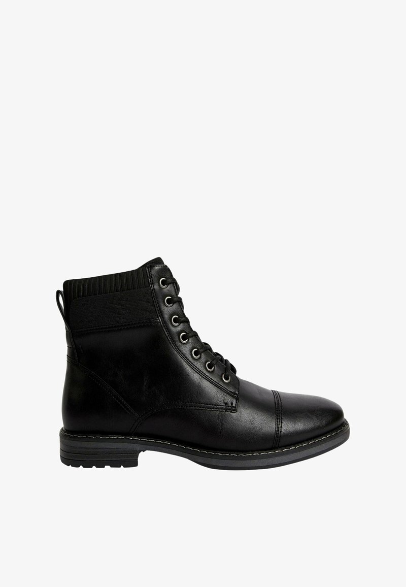 Bottine montante en cuir noir à lacets, avec col rembourré, œillets métalliques et semelle cousue sur fond blanc.