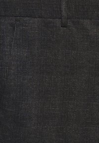 Tissu à carreaux noir avec un motif texturé, présentant un design subtil en grille. Le matériau semble tissé avec une finition douce.