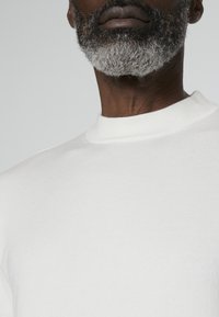 Pull blanc en maille côtelée à col rond, fabriqué dans un tissu doux et léger ; il présente une texture lisse et un détail de couture subtil au niveau du col.