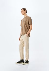 Bruine katoenen oversized t-shirt, beige tapered broek met elastische manchetten, en zwarte high-top sneakers met crèmekleurige zolen. Minimalistisch ontwerp en neutrale kleuren.