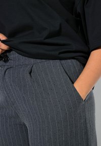 Šedé proužkované kalhoty z texturované látky, s knoflíkovým zapínáním a bočními kapsami, v kombinaci s černým topem.