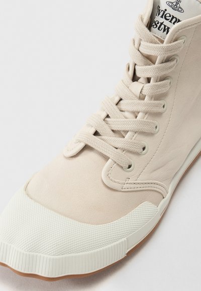 Höga sneakers i ljusbeige läder med en texturerad gummitå och kontrasterande vit sula, utrustad med platta skosnören och metallöglor.