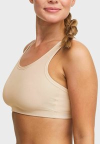 Ljust beige sportbh med en slät, strukturerad textil. Har breda band, rund halsringning och en figurnära design med minimala sömmar.