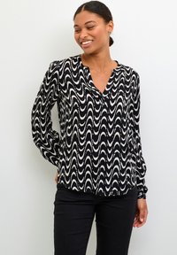 Blusa a righe in bianco e nero con maniche lunghe, scollatura a V e tessuto leggero. Abbinata a pantaloni neri.