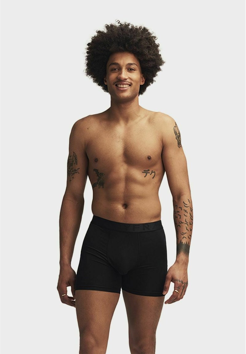 Svarta boxerkalsonger med resårmidja, modellen har en muskulös kropp och synliga tatueringar på armarna. Bakgrunden är helt vit.