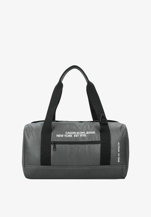 Bolsa de deporte gris con correas negras, que cuenta con un bolsillo con cremallera y una marca blanca. Fabricada con un tejido duradero y de textura suave.