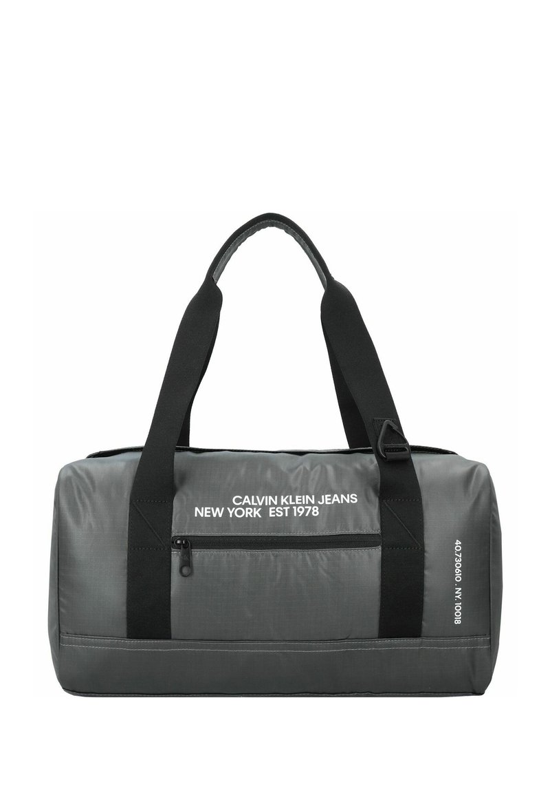 Bolsa de deporte gris con correas negras, que cuenta con un bolsillo con cremallera y una marca blanca. Fabricada con un tejido duradero y de textura suave.