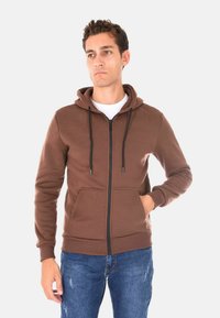 Felpa marrone con zip, cappuccio, lacci e tasca frontale. Realizzata in materiale morbido con polsini a coste e finitura liscia.